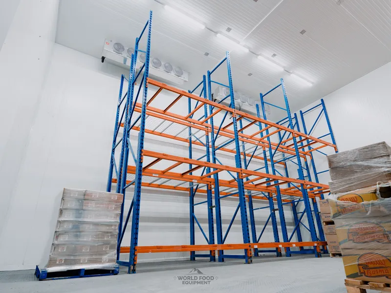 Industrial cold storage envelope at Atlas Foods with tall orange pallet racking installed, ceiling-mounted KeepRite evaporators, and stacked panel beam sections on the floor, World Food Equipment install, Ontario
